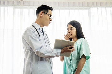Asian male doctor wearing stethoscope and holding a clipboard  checkup the symptom of female patient sitting on hospital bed