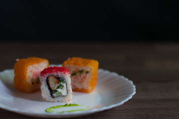 sushi with caviar, chicken, vegetables, cream cheese and wasabi on a white plate on dark background front view   