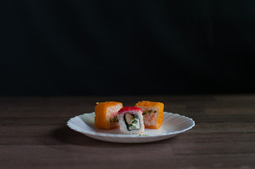 sushi with caviar, chicken, vegetables, cream cheese and wasabi on a white plate on dark background front view   