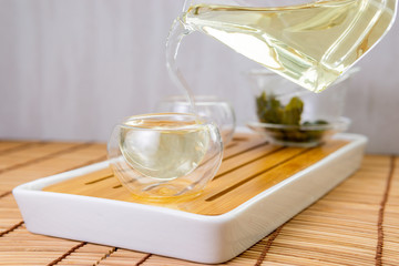 pours chinese green tea from glass kettle to small cup. close up selective focus