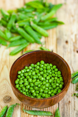 closeup green peas in brown dish, on wooden table.