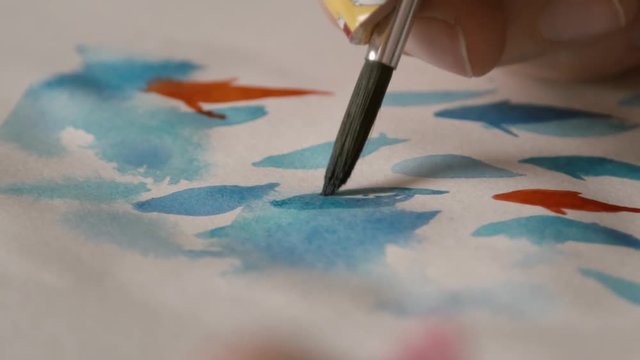 girl with a brush for painting in hands paints in a notebook watercolor drawing close-up