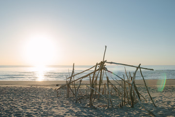 Seaside landscape in evening. Hut of branches on a beach. Relax in evening on the beach. Sunset at sea. Calm and sort seascape. Shelter of branches on the sand on the sea coast. 