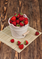 Red strawberies in a white bowl on the wooden table