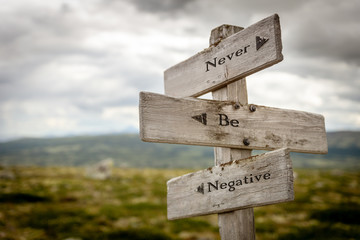 never be negative text engraved on old wooden signpost outdoors in nature. Quotes, words and illustration concept.