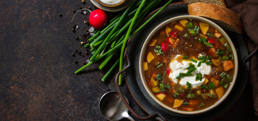 Traditional dish Russian cuisine. Cold summer Okroshka soup with kvass, sausage and vegetables in a bowl on a dark stone countertop. Top view flat lay background. Banner.