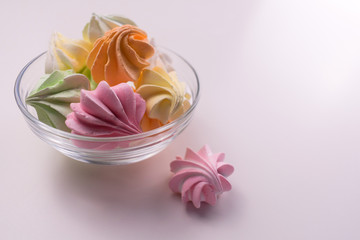 Multi-colored small meringues in a glass plate on a white background. Copy space.