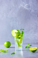 Mojito cocktail with lime and mint in tall glass. Fresh mojito in glass on a gray background. Refreshing mint cocktail with lime. Infused water