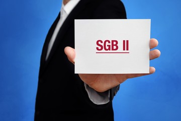 SGB II. Anwalt hält Karte in der Hand. Beschriftung auf Schild zeigt Begriff. Hintergrund blau....
