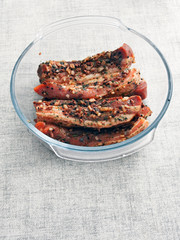 Pork belly slices marinated in soy sauce and herbs in a glass bowl on a light table cloth.