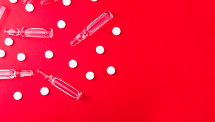 
Ampoules for injections and white pills on a bright red background. Medical background. Copy space. Flat lay.