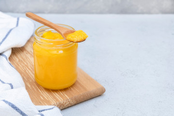 Glass jar of clarified butter (ghee) with wooden spoon on neutral concrete background. Image with copy space