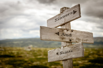 sinners and saints text engraved on old wooden signpost outdoors in nature. Quotes, words and...