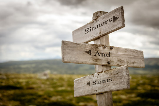 sinners and saints text engraved on old wooden signpost outdoors in nature. Quotes, words and illustration concept.