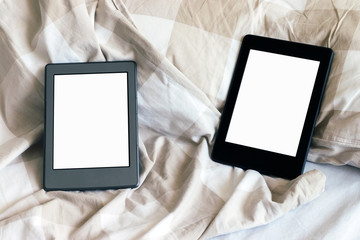 Two modern electronic books with a blank screens on a white and beige bed. Mockup tablets on bedding