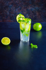 Mojito cocktail with lime and mint in tall glass. Fresh mojito in glass on a dark background. Cocktail with lime. Infused water. Copy space