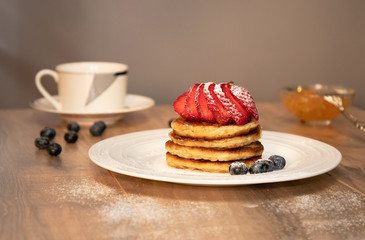 Pancakes with beries sprinkled with sahor powder, cup of tea and jam on the wood table