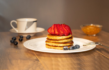 Pancakes with beries, cup of tea and jam on the wood table
