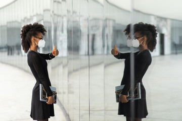 Successful stylish businesswoman with n95 face mask doing thumbs up gesture to herserlf in glass...