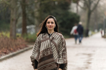 Fototapeta premium Young woman posing on park road dressed in poncho. Front view. Looking away.