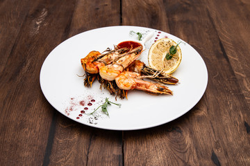Grilled tiger prawns with garlic, lemon and pepper in Thai sauce in a white plate on a wooden table.
