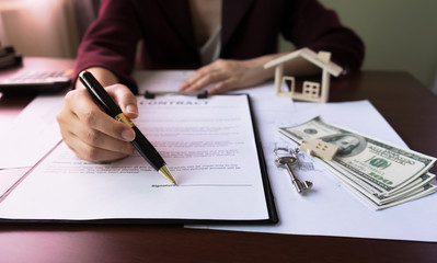 Real Estate Agent's Hand pointing signature Client in Contract Form on table with money, purchase agreement, house key, design home document. Concept of Investment property.