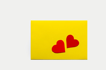 A yellow rectangular envelope and two red hearts on it. On a light background. With place for text.