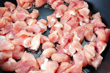 raw sliced small pieces of pork meat are fried in a pan in olive oil. close up selective focus