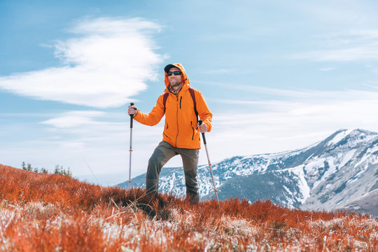 Dressed bright orange jacket backpacker walking by red blueberry field using trekking poles with mountain range background, Slovakia. Active people and European mountain hiking tourism concept image.