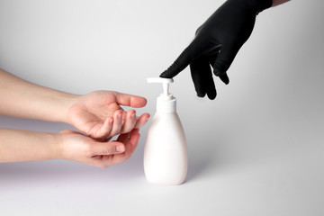 Someone in a black nitrile glove gives a disinfectant gel to the hands of another person without gloves