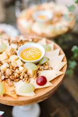 Patry finger food on cutting board snacks for wine on wooden cutting board. Various cheeses, nuts, honey and grapes