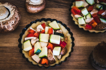 Prepared raw vegetable tartlets in black tart dishes on a wooden table.