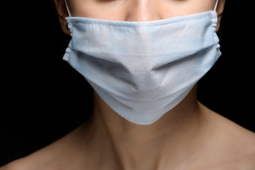 Protection against contagious disease, coronavirus. Female is wearing hygienic face surgical medical mask to prevent infection, respiratory illness as flu, 2019-nCoV. Studio photo black background