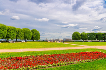 Strelka Arrow of Vasilyevsky Island with flowerbed, benches on green grass lawn and trees in Saint Petersburg (Leningrad) city, cloudy sky background, Russia