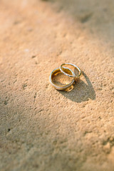 A pair of minimalist gold rings on a stone texture in the rays of the sunset. Wedding concept
