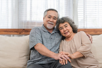 Lovely couple Asian elder happy and holding hands sitting together on the sofa at home