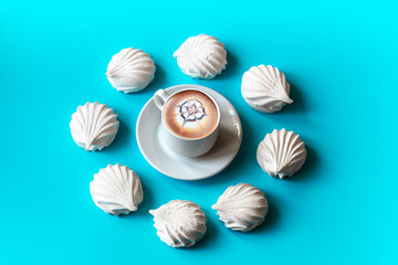 white vanilla marshmallows arranged in a circle on a blue background and in the middle a cup of cappuccino coffee