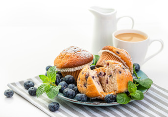 Blueberry Muffinson on a blue plate, fresh blueberries and coffee with cream in a white cup