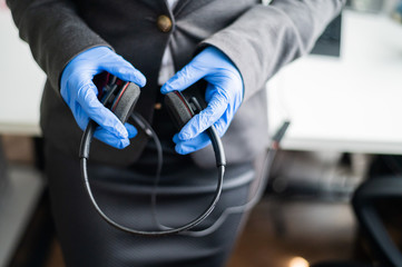 Close-up of female hands in gloves. Unrecognizable call center operator holding a headset. Office work concept during a pandemic. A method of protection against microbes.