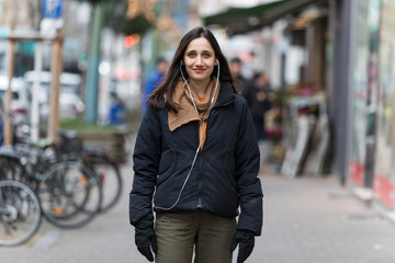 Young Indian woman dressed in autumn clothing and with earphones smiling at camera.