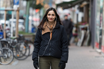 Fototapeta premium Young middle eastern woman dressed in autumn clothing and with earphones looking at camera.