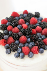 the tip of the white creamy open cake with a mix of wild berries - blueberry, raspberry, mulberry on white table