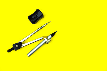 Black color pencil sharpener placed beside a compass attached to a silver pencil