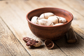 Dried organic Pecan nuts in orange ceramic bowl closeup. Studio macro shoot. Black concrete background