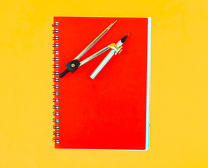 A red paper diary placed beneath a compass attached to a silver color pencil