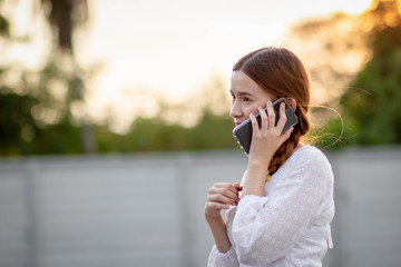 Displeased  and disappointed girl with a mobile phone stands in parking lot . In the evening the sunset was orange. copy space.