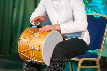 Crop of a caucasian man in a ethnic costume sits on a chair and plays the drum with his hands....