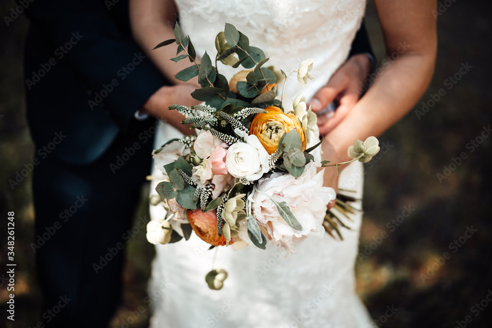 Wall mural photo of a bride with bouquet and the groom in the garden