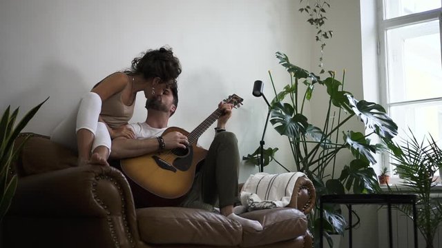 attractive middle age woman kisses man while he plays guital Spbd. emotional playing of a song for loved girlfriend. couple kissing. concept learning, romantic, in apartment.
