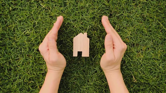 Hands protect Wooden house on green grass, Eco house concept.